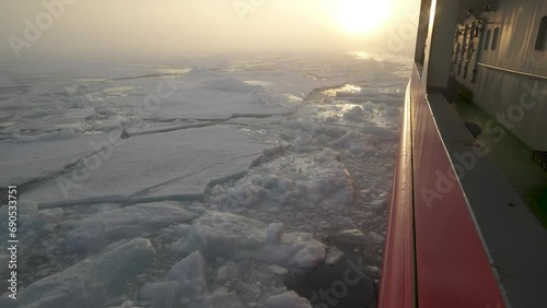 View from side of icebreaker back. Sun behind in fog. Pieces of ice float out from under side of ship. photo