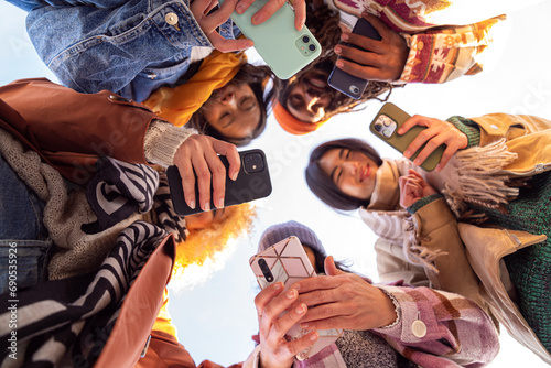 hands of different young people together forming team and unity multi ethnic group of boys and girls using smartphone shot from below autumn season