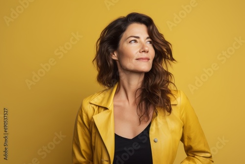 Portrait of beautiful woman in yellow jacket looking up on yellow background © Nerea