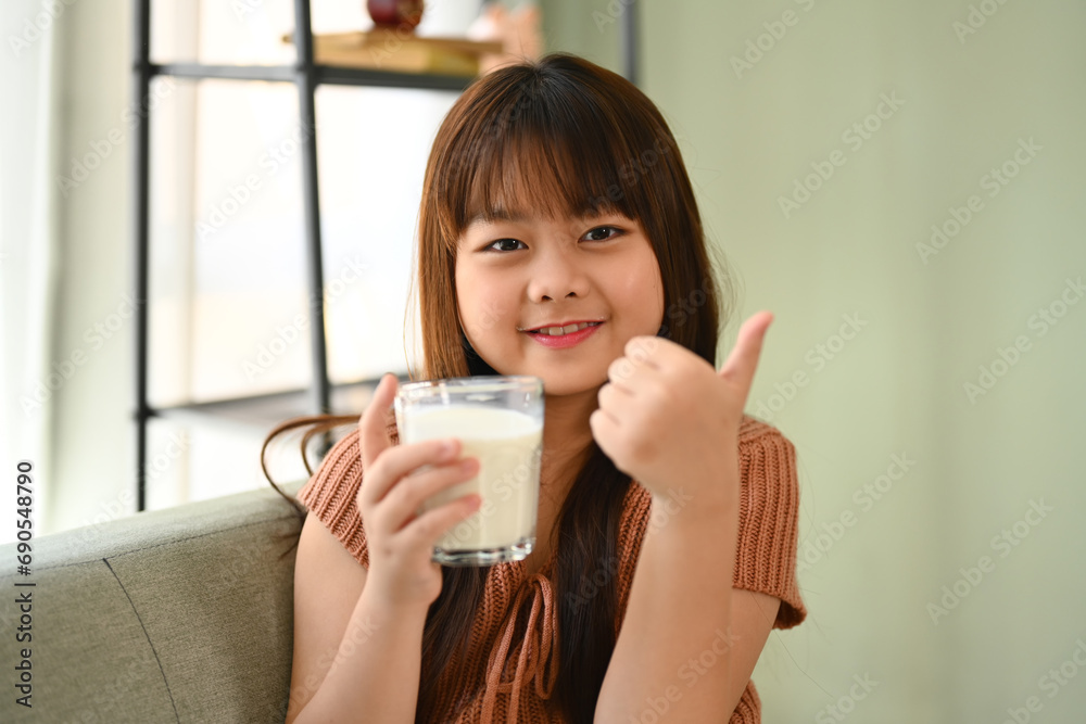 Happy Asian child holding a glass of milk and showing thumb up. Growth and nutrition concept. Happy Asian child holding a glass of milk and showing thumb up. Growth and nutrition concept.