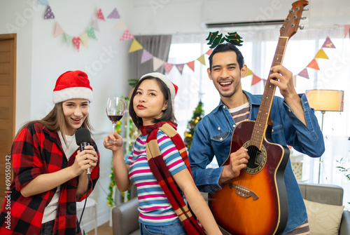 Happy friends celebrating Christmas together.Asian man playing guitar in living room full decoration with Xmas tree.
