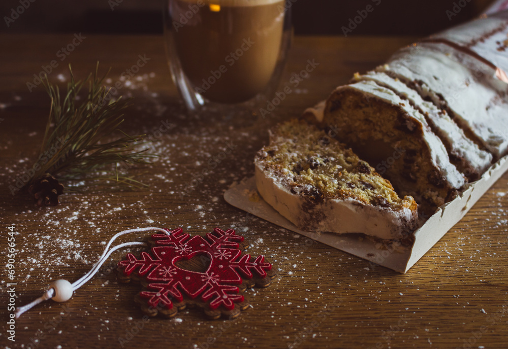 Christmas stollen with coffee cup and decoration toys. Sweet Christmas bread with cacao and powdered sugar. New Year decor. Homemade stollen with raisins on festive table. Winter breakfast. 