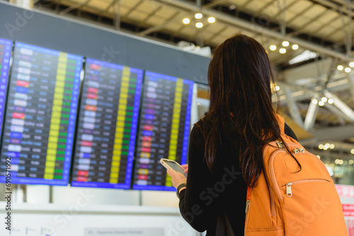 Photography Asian woman traveller with backpack checking a departures board at the airport terminal hall
