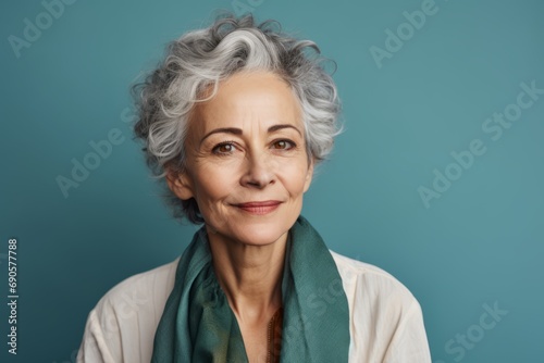 Portrait of senior woman with grey hair and green scarf on blue background