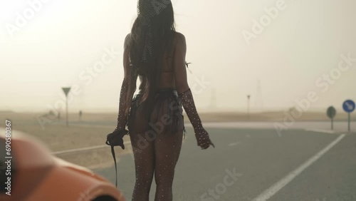 Young swarthy woman in a sexy outfit leads an expensive sports car on the road in the desert photo