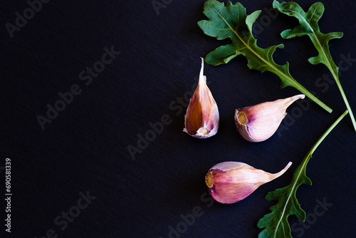garlic cloves and leaves of arugula on a black stone board, top view, copy space