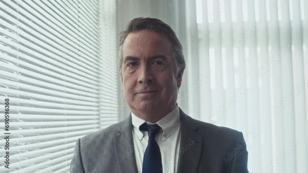 Medium shot of mature office worker in business suit standing next to window and looking at camera Medium shot of mature office worker in business suit standing next to window and looking at camera