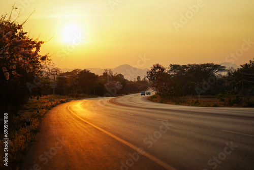 Country road with moving cars and beautiful golden sunset background in Thailand.