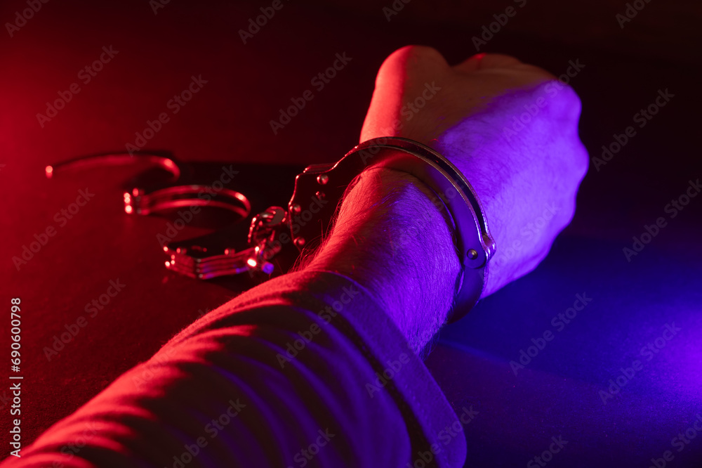 Male hand in handcuffs at night with police car lights