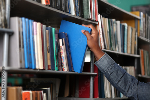 In a modern bookstore, the customer takes the book he likes off the shelf. Close-up of an African man's hand selecting a book to study in the library.