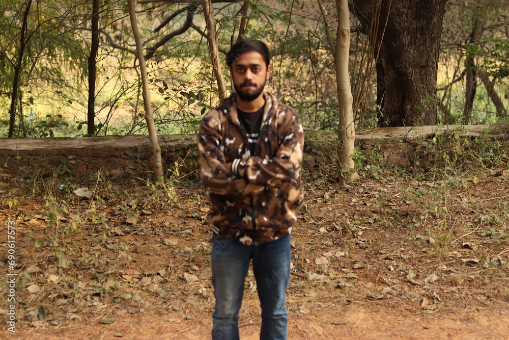 An Indian boy wearing camouflaged jacket with green trees and vegetations in the background