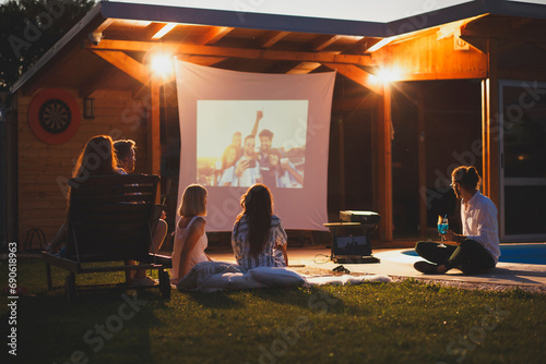 Friends having fun in home backyard open air cinema watching a movie photo