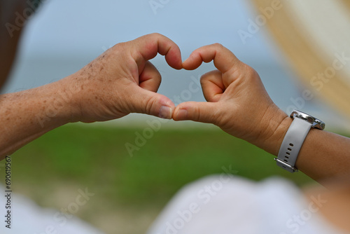 Close-up and Rear view with Elderly Asian couple making head shapes with their hands together in front of the beach © saltdium
