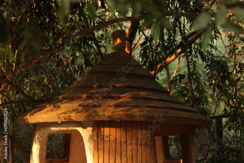 Upper half shot of A traditional grass and bamboo Indian rice cylinder round hut surrounded by green plants and trees in sunlight of golden hour photo