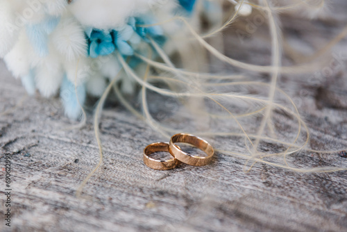 Stylish rings, bouquet of white and blue flowers on a wooden background. Rings for the bride and groom. Vows. Engagement. Luxury marriage and wedding accessory concept. Side view. Winter style.