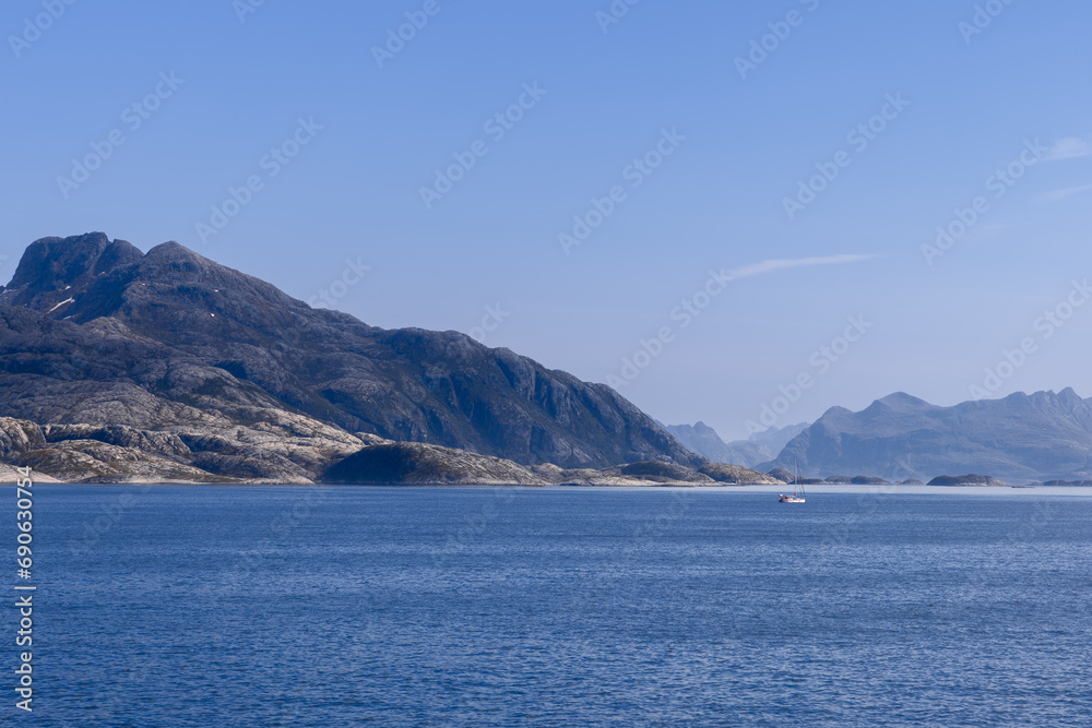 A picturesque view of the North Sea with a solitary, sculpted mountain towering over tranquil waters, featuring a sailing boat near Lofoten Island A picturesque view of the North Sea with a solitary, sculpted mountain towering over tranquil waters, featuring a sailing boat near Lofoten Island