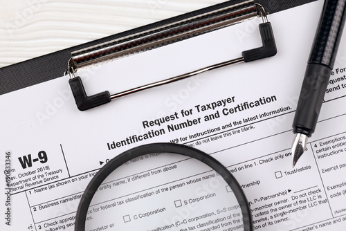 IRS Form W-9 Request for taxpayer identification number and certification, blank on A4 tablet lies on office table with pen and magnifying glass close up