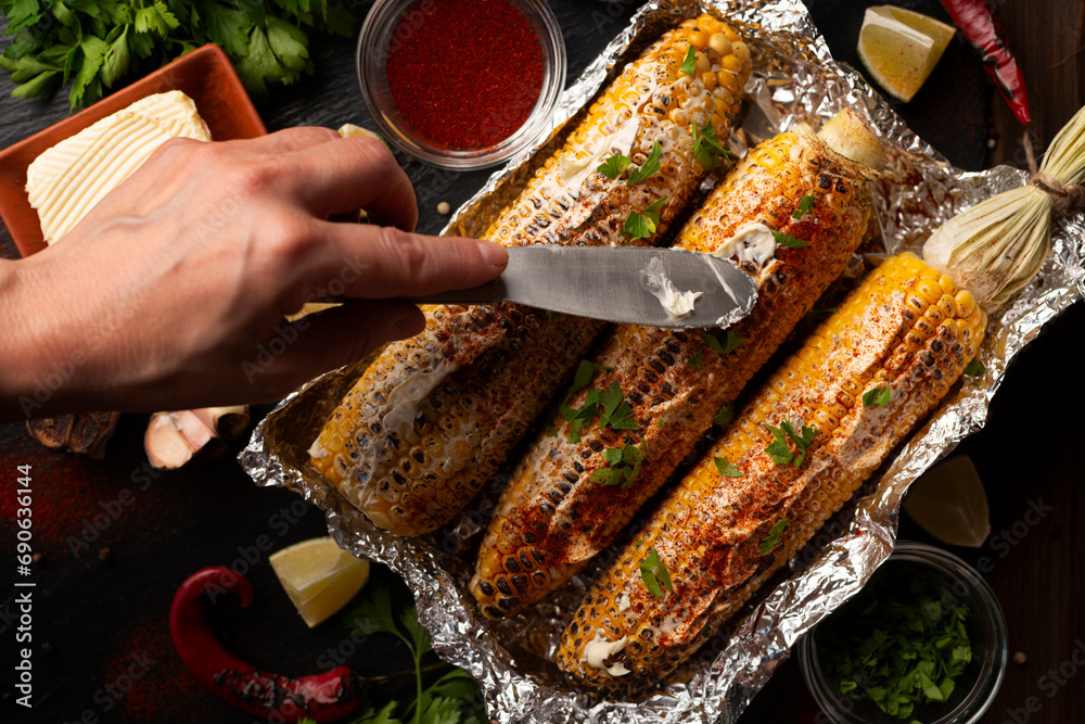 Grilled Sweetcorn with smoked paprika lime and butter on kitchen table being seasoned with table knife flat lay view