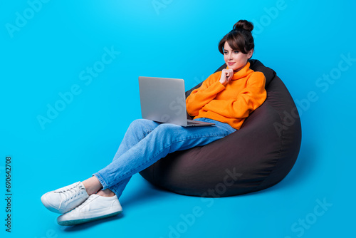 Photo of cheerful smart lady wear knitted pullover sitting bean bag hand arm chin reading modern gadget isolated blue color background