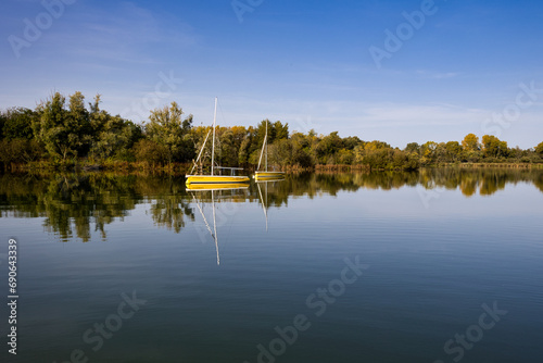 petit bateau  de plaisance jaune sur un lac avec un ciel bleu  et qui ce reflète dans l eau