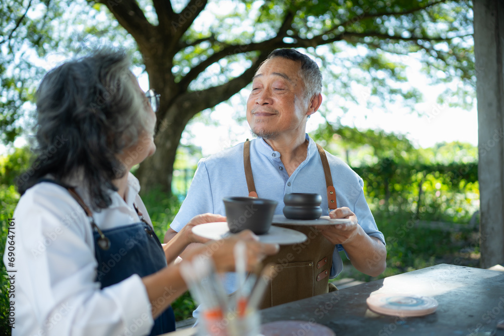 In the pottery workshop, an Asian retired couple is engaged in pottery making and clay painting activities. In the pottery workshop, an Asian retired couple is engaged in pottery making and clay painting activities.
