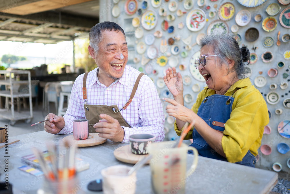 In the pottery workshop, an Asian retired couple is engaged in pottery making and clay painting activities. - obrazy, fototapety, plakaty 