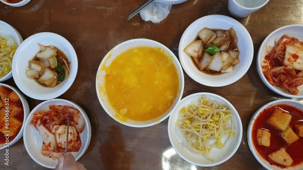 Hand eating Korean food banchan side dishes and Hobakjuk Pumpkin Porridge top view hands with chopsticks Hand eating Korean food banchan side dishes and Hobakjuk Pumpkin Porridge top view hands with chopsticks
