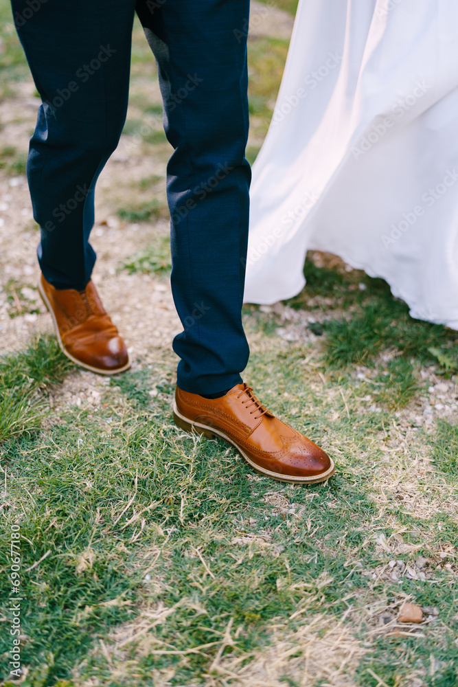 Groom in brown brogues walks next to the bride in a white dress. Cropped. Faceless