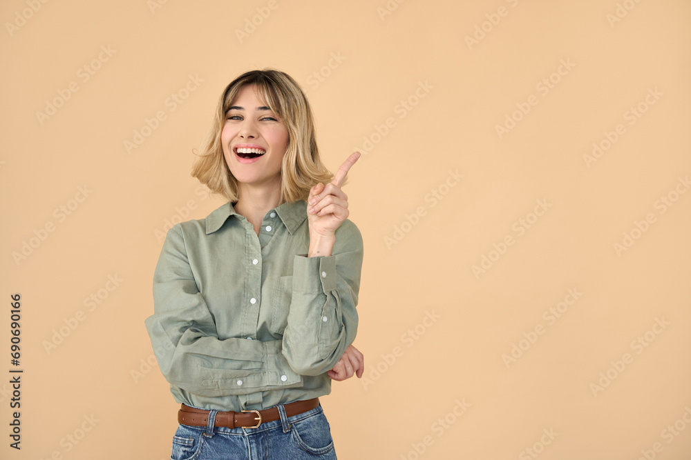 Obraz premium Happy pretty gen z blonde young woman, smiling student girl with short blond hair wearing shirt and jeans pointing aside presenting promotion laughing standing isolated on beige background. Copy space