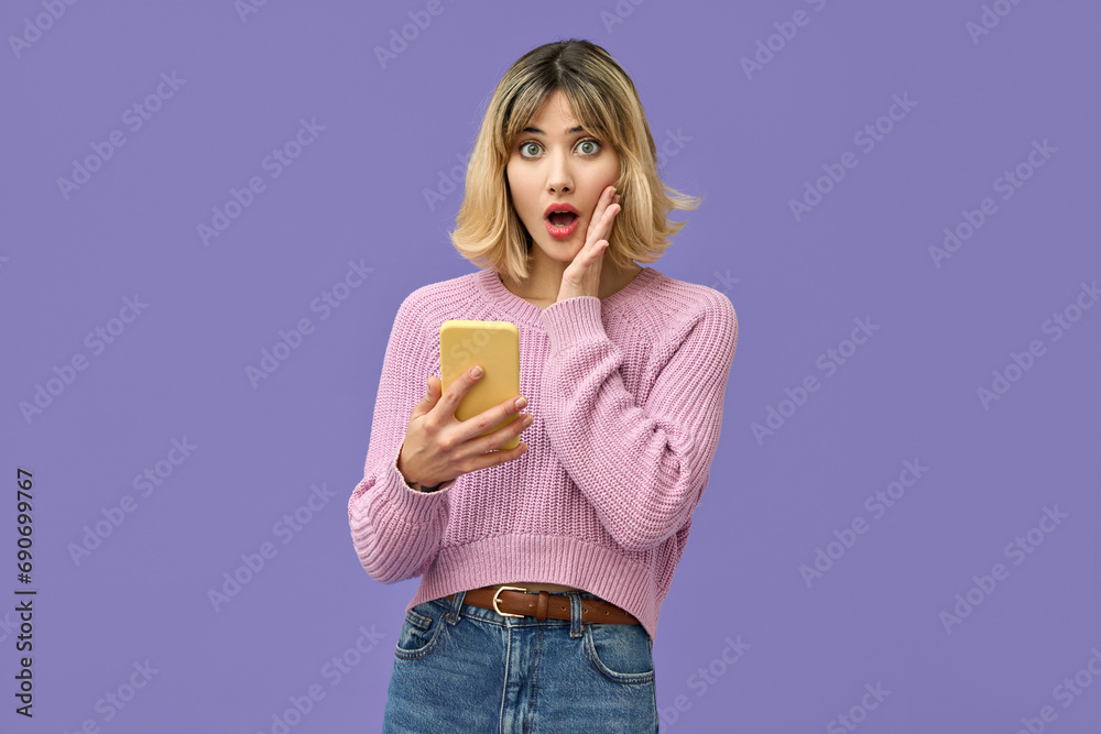 Shocked young gen z blonde woman shopper holding smartphone using mobile cell phone surprised about wow fashion sale app, omg promo discounts on cellphone isolated on purple background. Shocked young gen z blonde woman shopper holding smartphone using mobile cell phone surprised about wow fashion sale app, omg promo discounts on cellphone isolated on purple background.