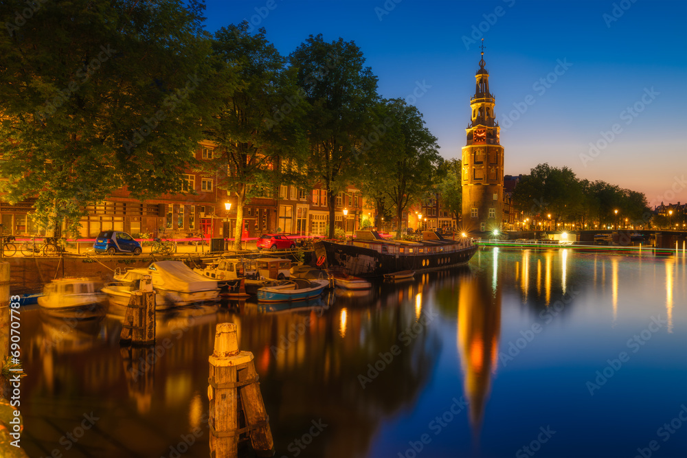 Montelbaan tower, Amsterdam, Netherlands. Evening cityscape. Dark sky and city lights. Dutch canals. Reflections on the surface of the water. Photography for design and wallpaper.