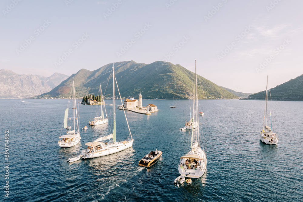 Motor yacht and sailboats sail along the Bay of Kotor to the island of Gospa od Skrpjela. Montenegro. Drone - obrazy, fototapety, plakaty 
