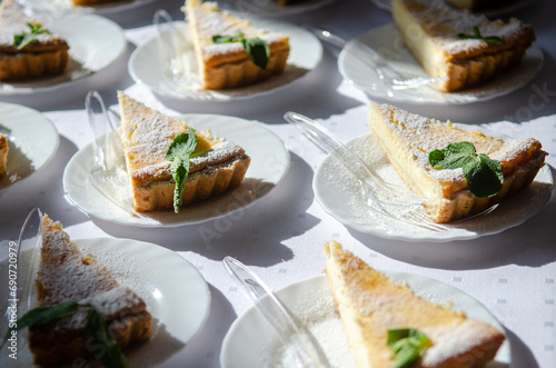 Triangular pieces of cheesecake with mint on white plates with forks, under the sun rays, catering at the event