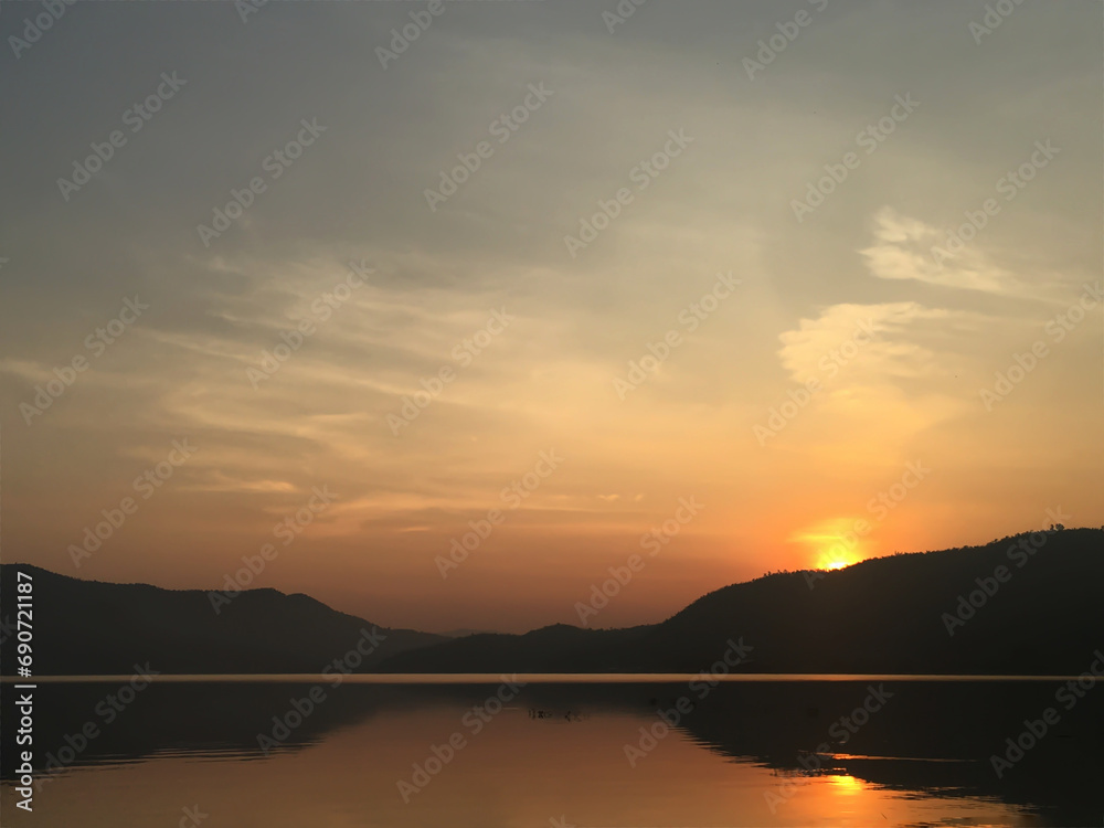 The sun was rising on the mountain top, reflecting orange on the water surface. The scenery is warm and relaxing.