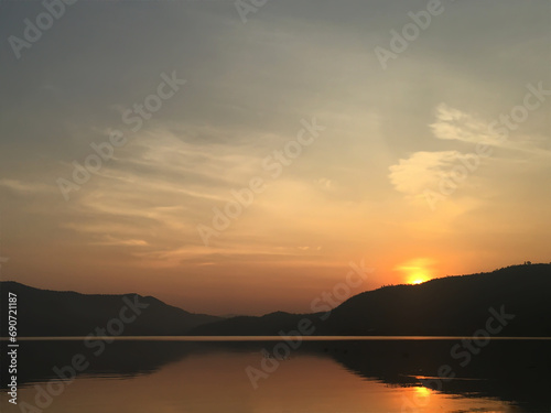 The sun was rising on the mountain top  reflecting orange on the water surface. The scenery is warm and relaxing.