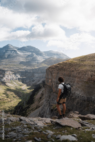mountaineer man with backpack observes the Ordesa Valley from the top of the canyon, during his adventure trekking