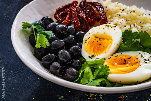 Boiled eggs with boiled white rice, sun dried tomatoes and green olives on wooden table
 photo