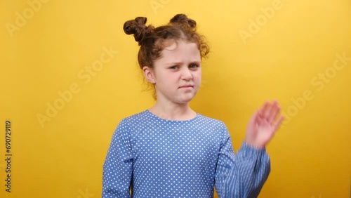 Portrait of disgusted little girl kid smelling stinky smell and frowning, angry looking at camera, standing posing over yellow color background wall in studio with copy space. People emotion concept photo