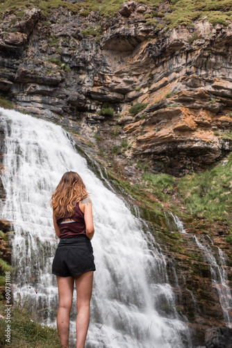 Young girl in front of a huge waterfall called Cola de Caballo in Monte Perdido national park while sightseeing in the Pyrenees in summer