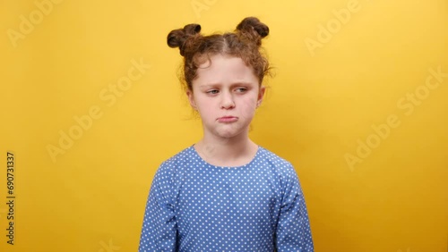 Misbehavior and childhood concept. Portrait of naughty upset little caucasian girl child sulking and grimacing expressing discontent, posing isolated over plain yellow color background wall in studio photo
