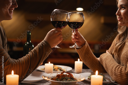 Happy young couple in love drinking wine and clinking glasses having romantic dinner