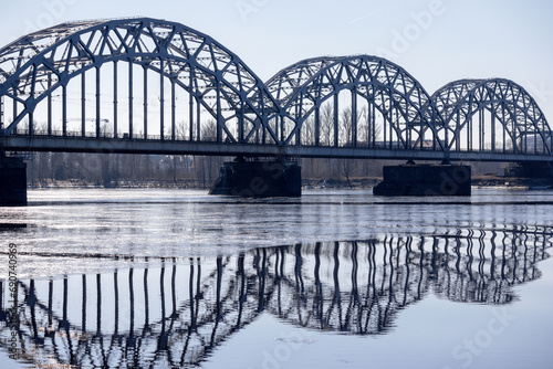 
A metal arched bridge across the river with the reflection of the bridge in the water in the form of an arch