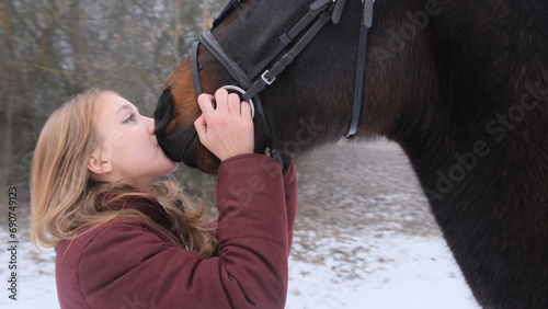 A beautiful teenage girl playfully kisses a brown horse in a foggy field.