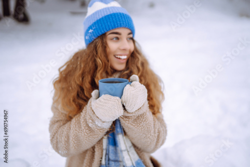 Smiling woman with a thermos in a snowy forest enjoying nature. Young woman drinking a hot drink outdoors. Adventure concept. Lifestyle. © maxbelchenko