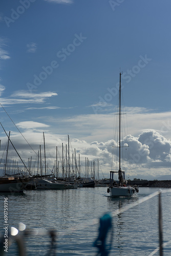 sailing boat approaches a serene marine setting against a backdrop of a clear blue sky. The boat sails gracefully upon the calm waters, creating a sense of tranquility and freedom