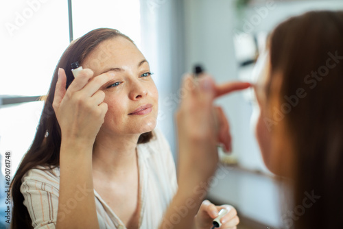 Young woman looking at mirror while touching her face applying moisturizer