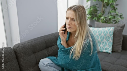 Attractive young blonde feeling the freezing chill, wrapped snugly in a warm blanket, feverishly talking on her phone from the cozy comfort of her living room couch at home. photo