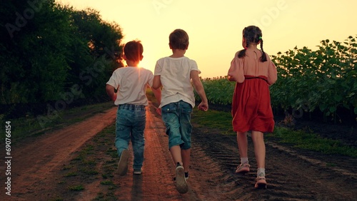 Kids play, run through field of sunflowers, friends run at sunset. Happy Children dream concept. Happy boy, girl running, playing together in nature. Family, children travel in nature. Brother sister