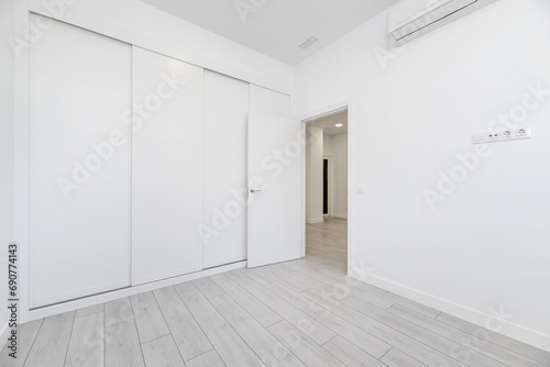An empty room in a loft-type home with a built-in wardrobe that covers the entire wall with white wooden sliding doors and an access door to the room made of the same material