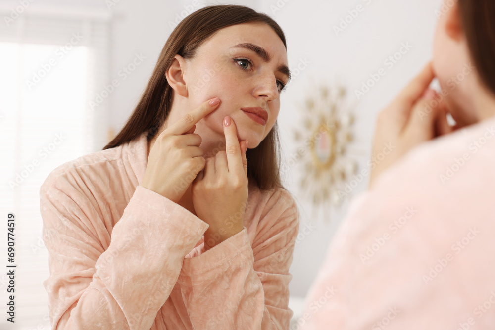 Young woman with skin problem looking at mirror indoors Young woman with skin problem looking at mirror indoors